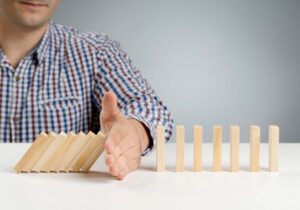 Hand preventing dominoes from falling, representing common mistakes to avoid in postgraduate applications – The Red Pen