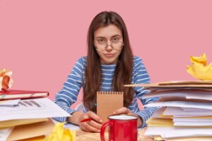 Student holding notebook amidst cluttered desk symbolizing common college essay mistakes – The Red Pen