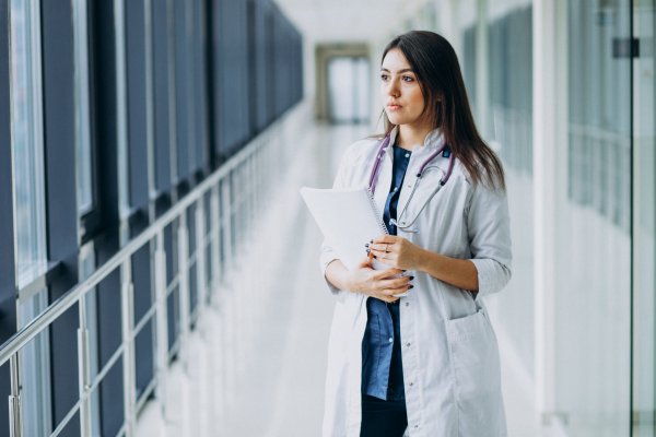 Young woman in a white lab coat with a stethoscope and clipboard studying medicine, showcasing UK medical schools - The Red Pen